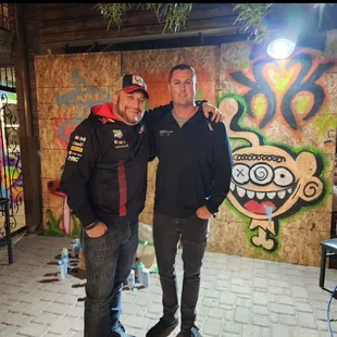 two men standing in front of a graffiti covered wall