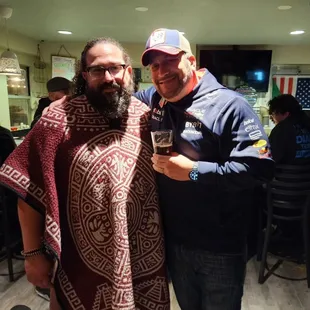 a man with a beard standing next to a man who is holding a glass of beer