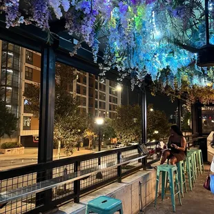 a woman sitting at a bar with flowers hanging from the ceiling