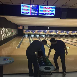 two men pushing a bowling ball down a lane