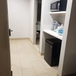 Mini fridge and coffee maker.  Coffee maker is encased in protective plastic for cleanliness