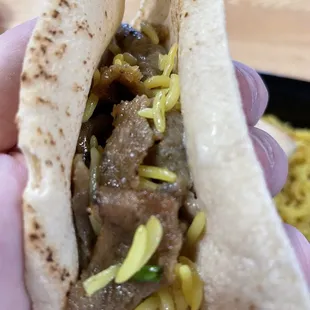 a hand holding a pita filled with meat and vegetables
