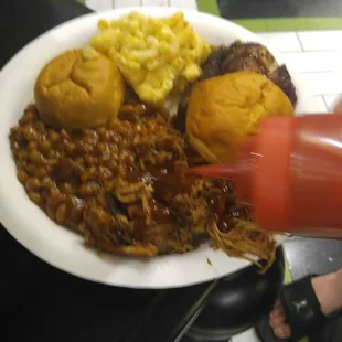 Full plate of pulled pork, Mac and cheese, baked beans, and bbq chicken legs. Pouring on extra bbq sauce.