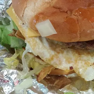Double cheese burger with a fried egg, onion straws, lettuce, tomato, and raw onions,
