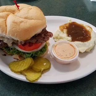 a hamburger with a side of mashed potatoes and pickles