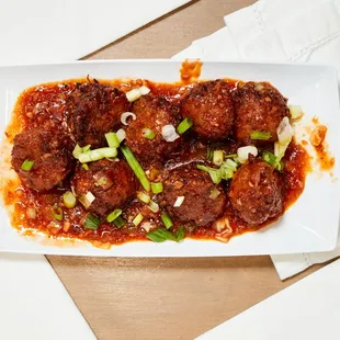 a plate of meatballs with sauce and green onions