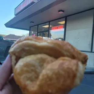 a person holding a pastry in front of a store