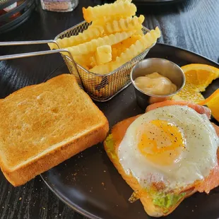 Toast with avacado, smoked salmon, and eff with french fries and orange slices.