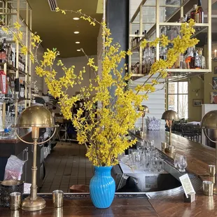 yellow flowers in a blue vase on a bar
