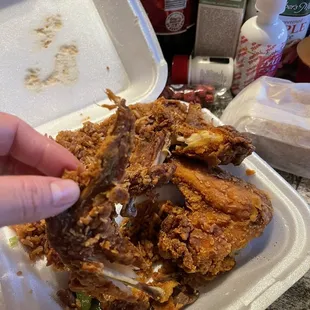 a person grabbing a piece of fried chicken from a styrofoam container