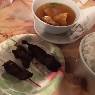 a bowl of soup and a plate of skewered meat