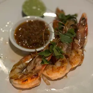 a plate of grilled shrimp with a side of dipping sauce