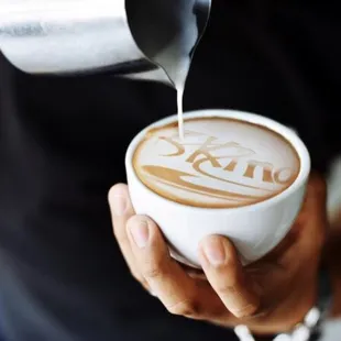 a person pouring milk into a cup of coffee