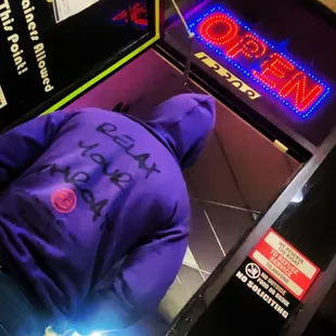 a person in a purple hoodie in front of a neon sign