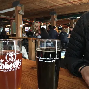 a woman sitting at a table with two pints of beer