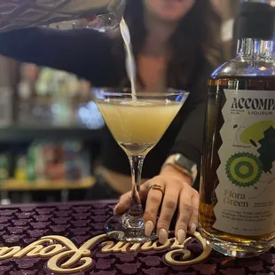 a woman pouring a drink into a martini glass
