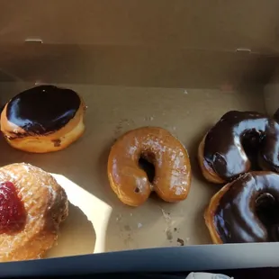 1 Boston cream (top left), 1 classic glazed (middle), 2 chocolate glazed (right side), and 1 cornbread with raspberry jelly (bottom left).