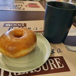 a glazed donut on a plate with a cup of coffee