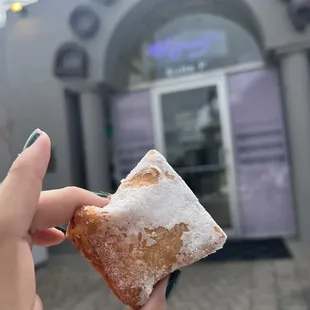a person holding a pastry in front of a building