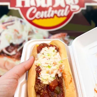 a person holding a hot dog in a styrofoam container