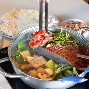 a person holding tongs over a pot of soup