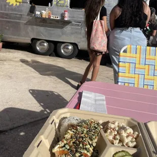 a hot dog, cucumbers, and pickles on a table in front of a food truck