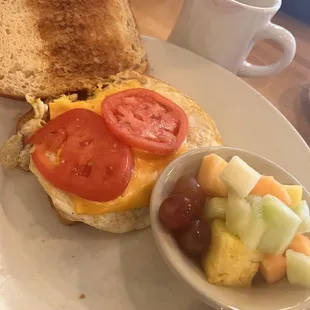Egg and cheese sandwich with tomato and Mayo on sourdough toast. With a side of fruit and a hot cup of coffee