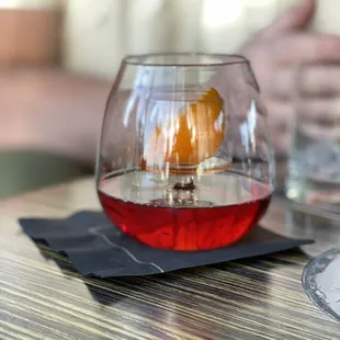a glass of red wine with a slice of orange in it