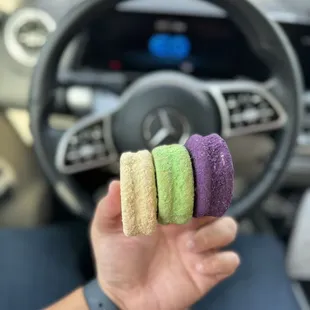 a person holding a car steering wheel with four colored cookies in their hand