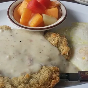 Country fried steak, overeasy eggs, and fruit.