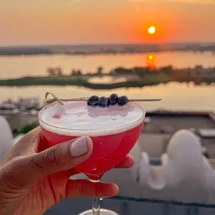 a person holding a drink with a sunset in the background