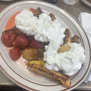 a plate of french toast, strawberries, and whipped cream