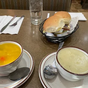 Chicken noodle soup and cream of potato soup, with dinner rolls.