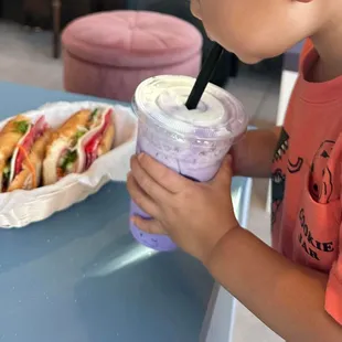 a young boy eating a sandwich and a drink