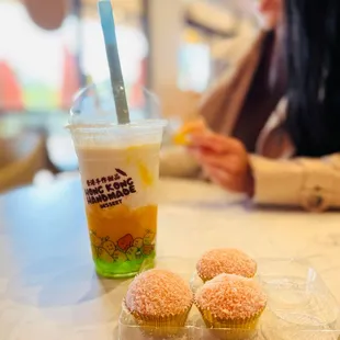 a woman sitting at a table with three cupcakes and a drink