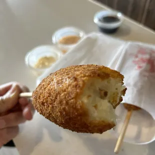a hand holding a fried donut with a bite taken out of it