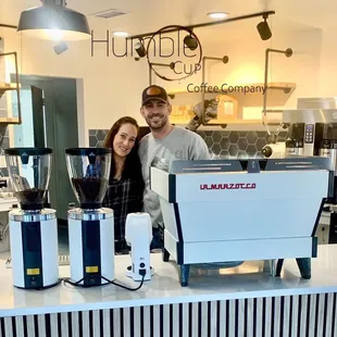 a man and a woman standing behind a coffee machine
