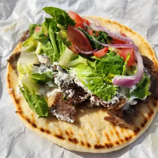 a pita with meat, lettuce, tomato, and onions