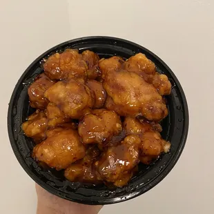 a hand holding a bowl of chicken wings