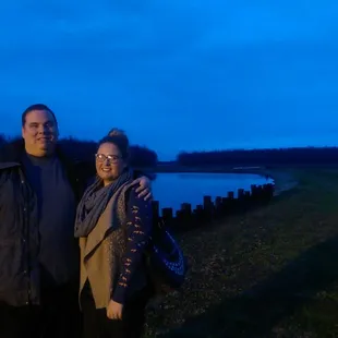 a man and a woman standing next to a pond