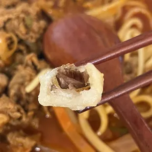 a piece of meat and noodles with chopsticks
