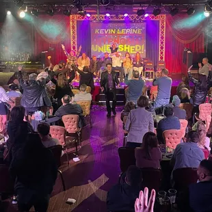 a crowd of people sitting at tables in front of a stage