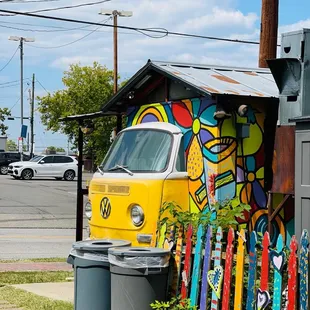 a yellow vw bus parked in front of a colorful fence