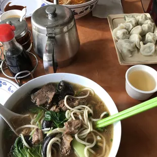 Beef stew noodles in foreground, half eaten spicy sliced beef noodles in the back, and pork and chive dumplings