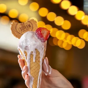 a hand holding a waffle cone with a strawberry on top