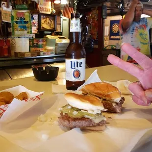 a man sitting at a bar with two sandwiches and a bottle of beer