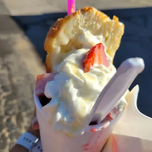 a hand holding an ice cream sundae with strawberries and whipped cream