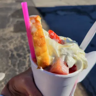 a hand holding a cup of ice cream and strawberries
