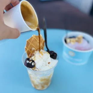 a person pouring syrup into a cup of ice cream