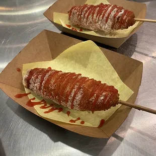 We now have Korean style corn dogs! In the photo there are two cheese Korean styled corn dogs with sugar and ketchup on top.